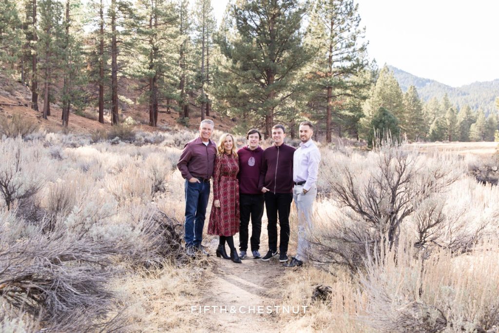 A family wearing burgundy poses for a mountain family portrait while standing on a trail that weaves through a lovely meadow