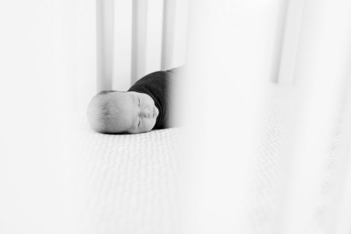 A black and white image of a baby boy swaddled in his crib as part of his casual reno lifestyle newborn photos