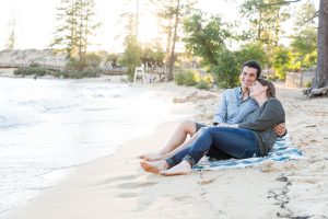 couple sits on the beach of Sand Harbor for their engagement session with Tahoe photographer