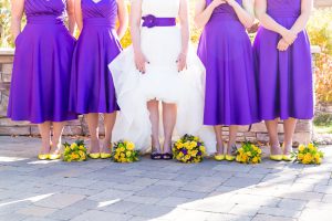 Bride and bridesmaids show off funky and vibrant colored shoes with their yellow and purple bouquets on the ground for wedding photos by Reno Wedding Photographer
