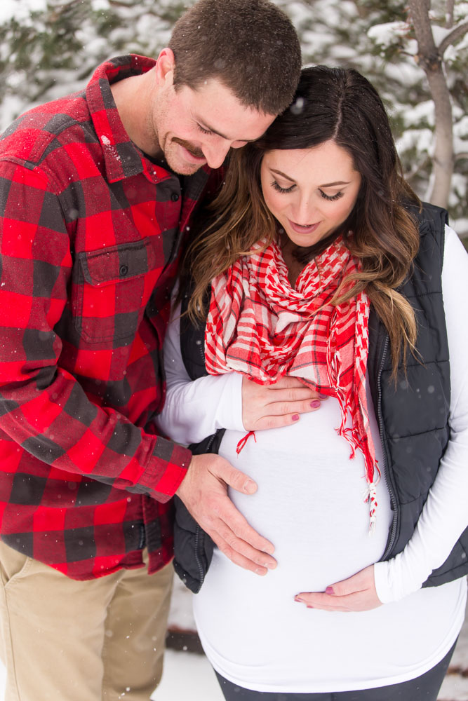 Husband hold wife's pregnant belly as they admire their son before he greets the world at Bartley Ranch in Reno for their snowy Reno maternity photos by Reno maternity photographer