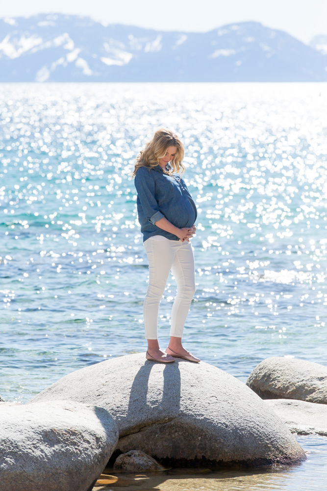 Stunning mama-to-be standing on rocks above lake tahoe for sunny spring maternity photos at Sand Harbor in Lake Tahoe by Lake Tahoe Maternity Photograhpher