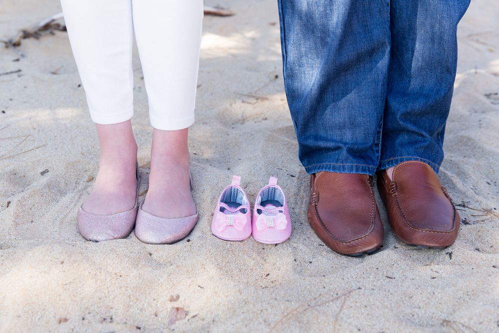 newborn baby girl shoes between mom and dad for sunny spring maternity photos at Sand Harbor in Lake Tahoe by Lake Tahoe Maternity Photograhpher
