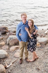 Sweet male and female couple smiling at the camera on the shore of Donner Lake for an engagement portrait by Lake Tahoe Wedding Photographer