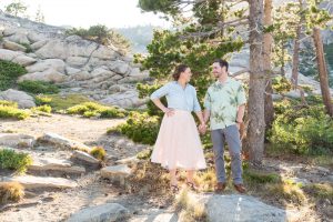 engaged couple looks at one another while standing on granite rocks above Donner Lake