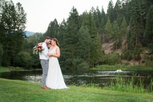 bride and groom smile in front of pond after sunset on their Greenhorn Creek Guest Ranch Wedding day