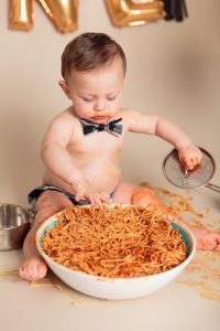 Baby boy plays with pan and spaghetti during his One Year Spaghetti Smash portrait session by Reno Baby Photographer