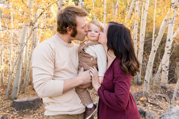 A mom and dad give their baby boy a kiss with beautiful golden aspens behind them at the Thomas Creek Trailhead