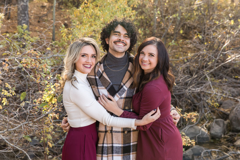 Three siblings embrace for Reno fall family portraits near Thomas Creek in Reno by Reno Family Photographer