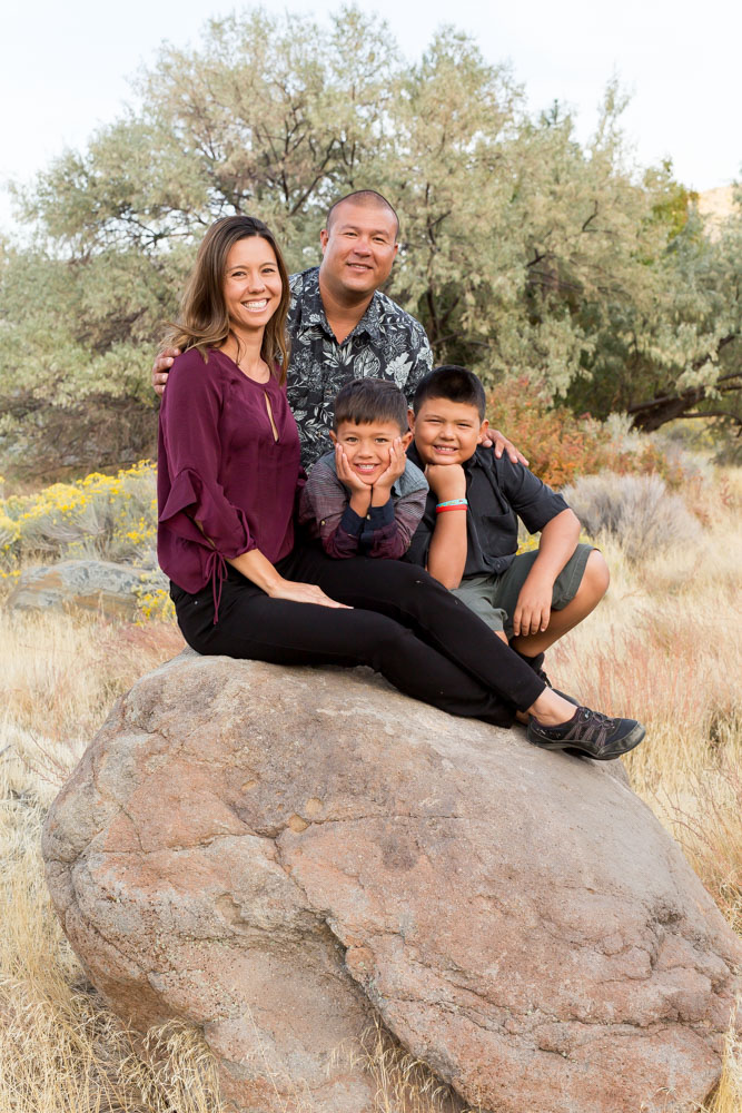 Family of four sits on a rock at Mayberry Park and smiles for Reno Family Photographer during fall family photos