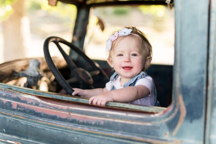 one year old baby girl stands inside a blue vintage truck for her reno one year portraits by Reno Child Photographer