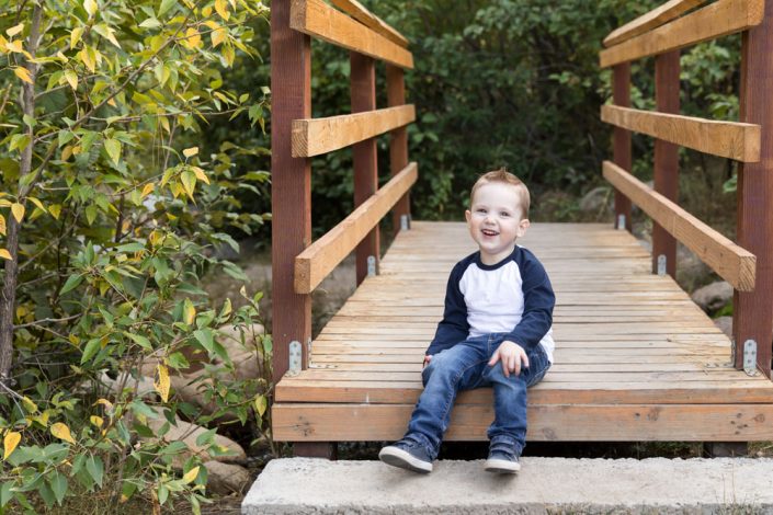3-year-old boy sits on a bridge at Galena Creek Park in the fall for child photos by Reno child photographer
