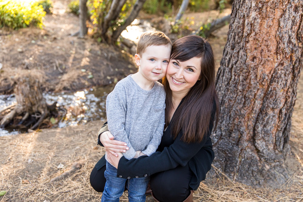 A mom snuggles her son by a creek during their fall family portrait session with Reno Family Photographer