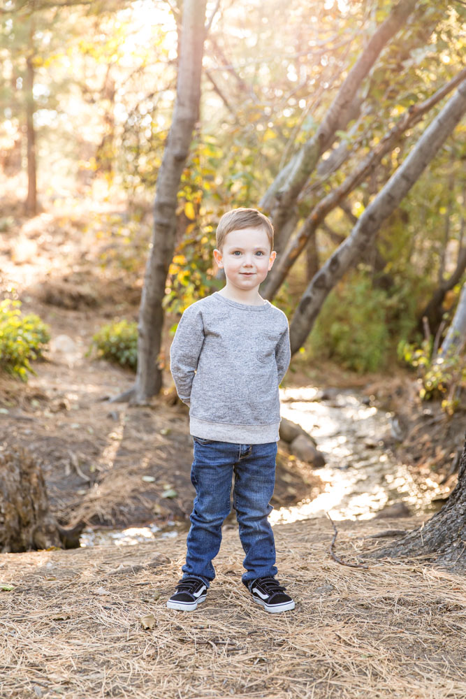 Cute four year old boy stands in front of a babbling brook for his Reno fall family portraits