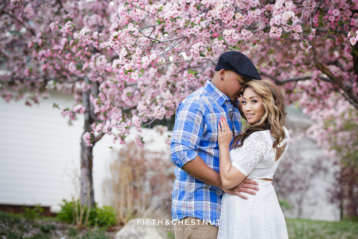 A couple lovingly holds one another with a bright pink blossiming tree in the background for Spring Reno Family Portraits by Reno Family Photographer at Rancho San Rafael