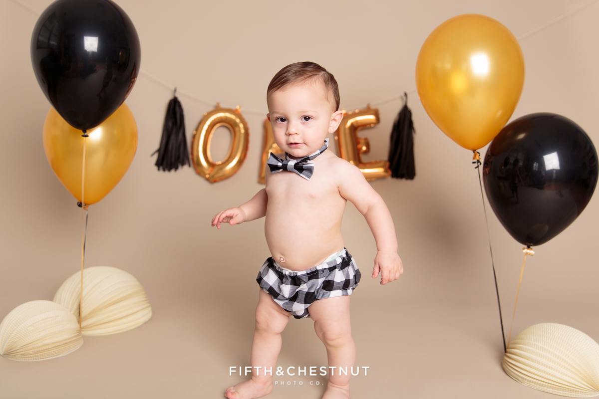 Cute baby boy standing among balloons for his one year spaghetti smash toddler portraits