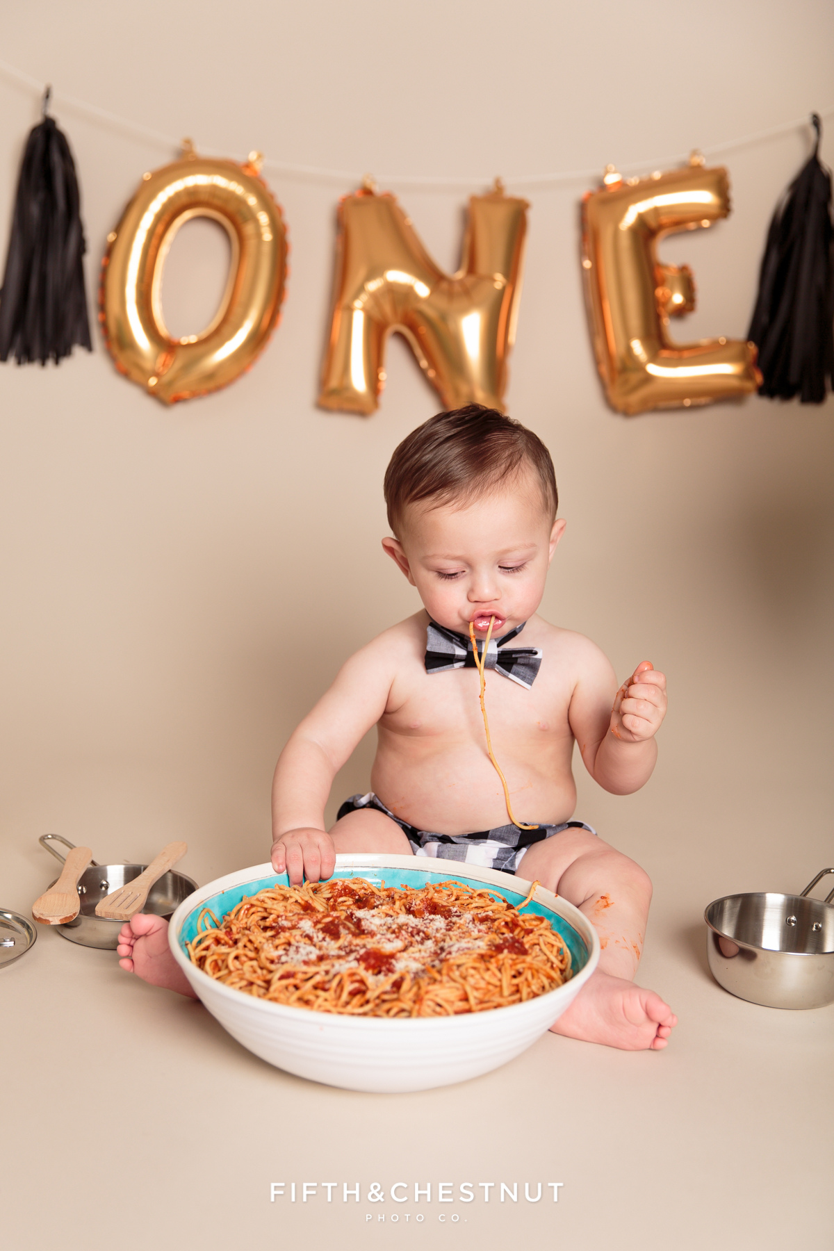 One year old boy digging into giant bowl of spaghetti during one year spaghetti smash toddler portraits