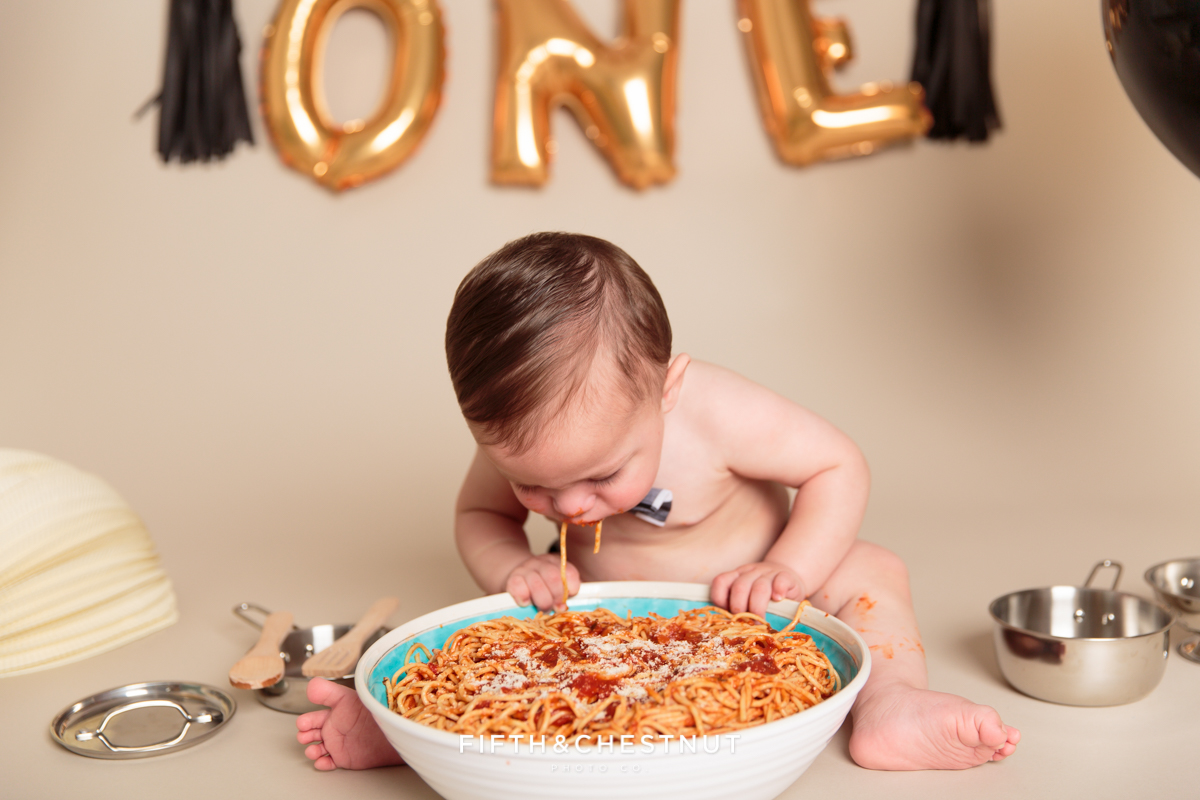 Baby boy smashing face into big bowl of spaghetti for his one year spaghetti smash toddler portraits
