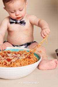 Toddler playing with spaghetti for a one year spaghetti smash portrait session
