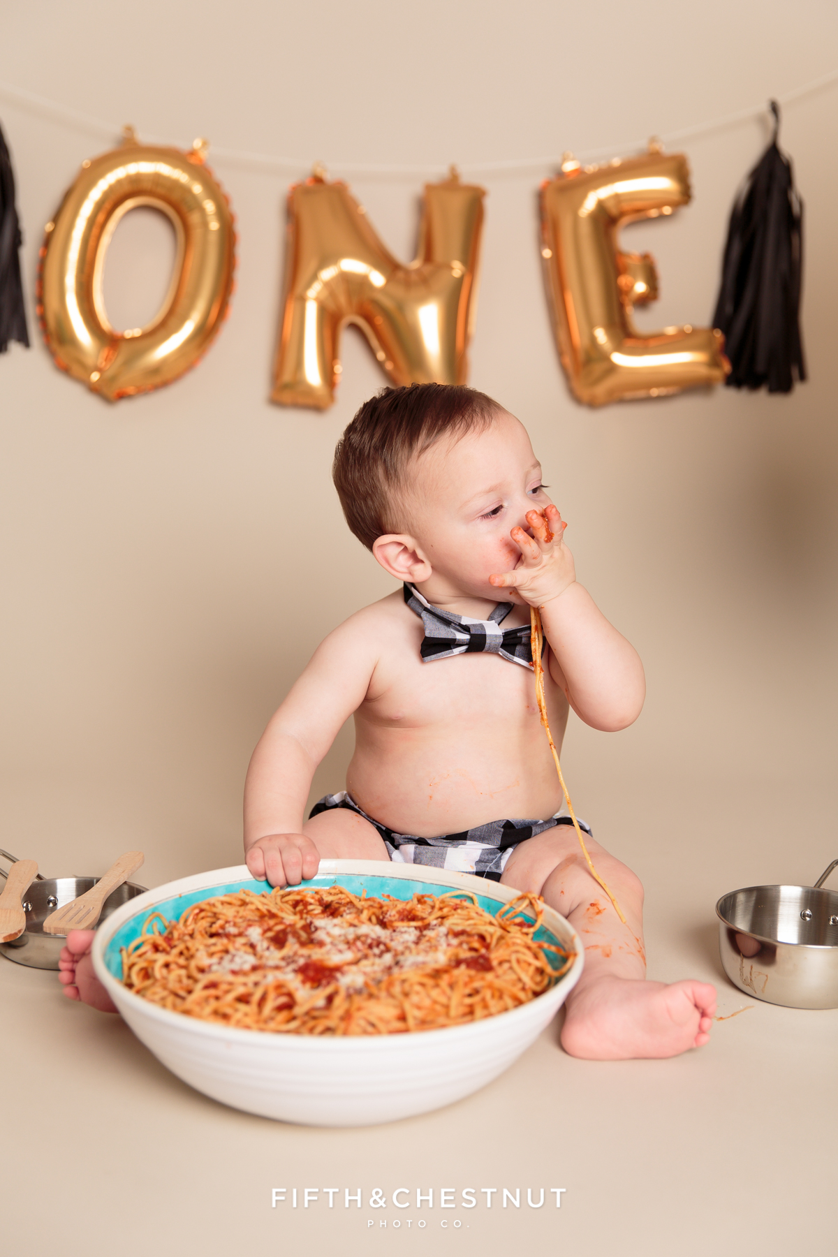 Baby boy wearing a bow-tie and diaper cover eating spaghetti