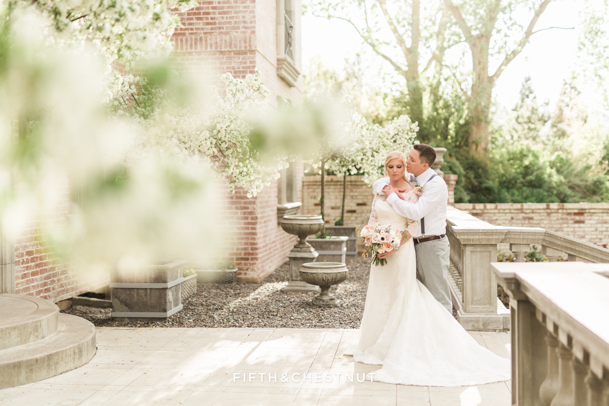 Bride and groom embrace on the blossom-lined front porch of a Reno brick and stone private estate