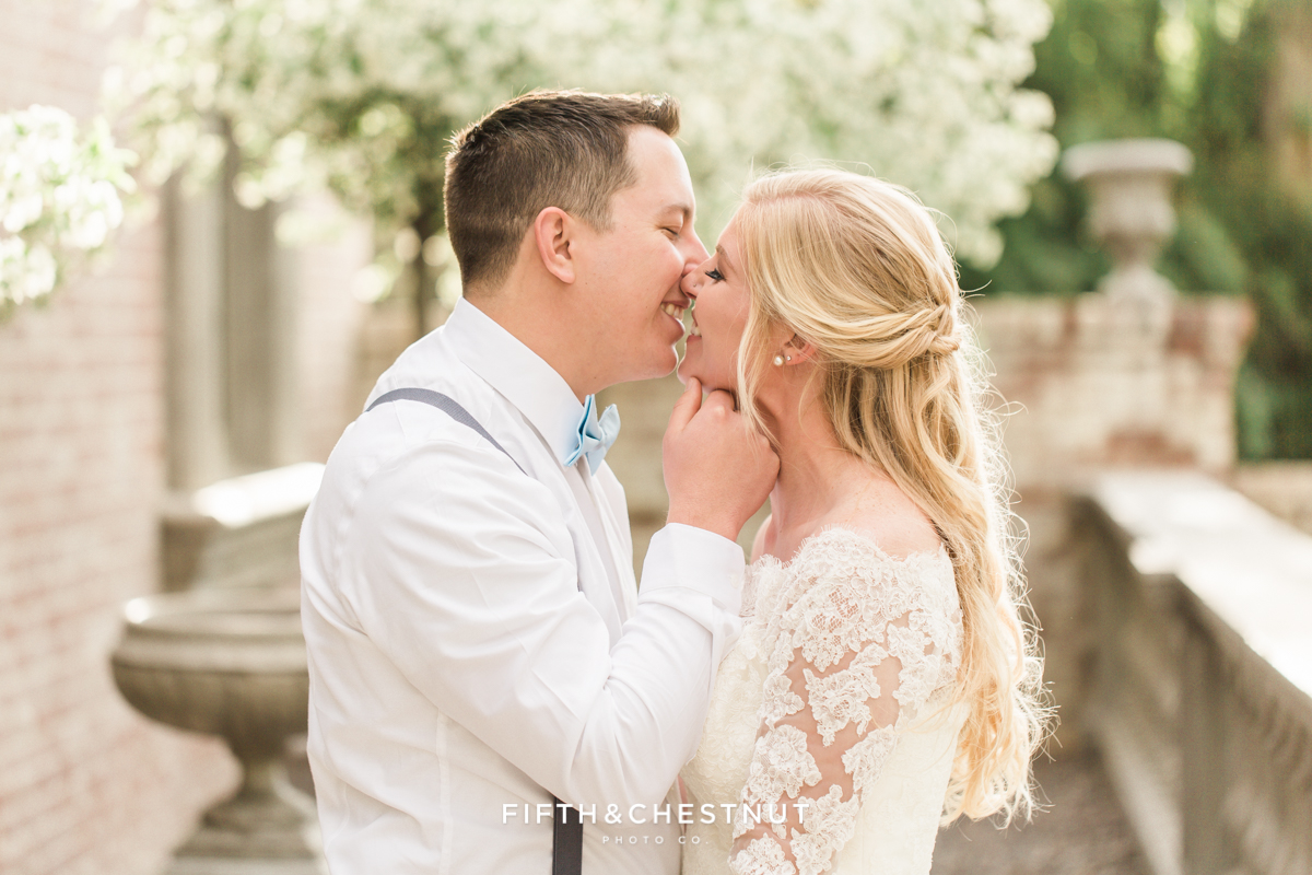 Bride and groom share a sweet kiss on a blossom-lined front porch of a brick private estate