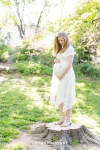 Pregnant woman standing on a log and looking down at her baby bump