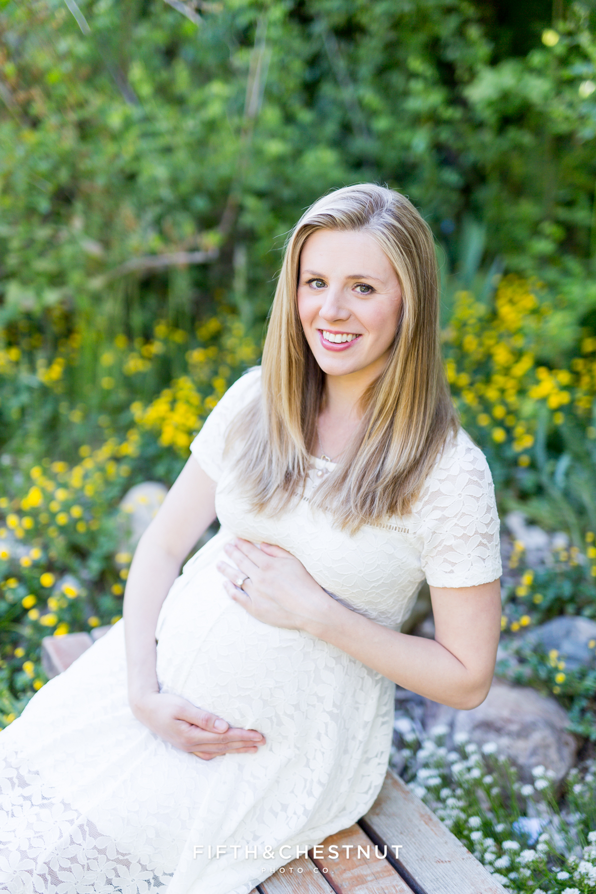 Happy pregnant woman smiling while holding her baby bump at Rancho San Rafael Park in Reno