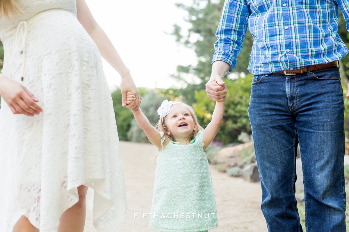 Portrait of happy smiling toddler in between her mom and dad while they hold hands