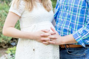 Husband and wife hold hands over pregnant belly for spring maternity portraits in Reno by Reno Maternity Photographer