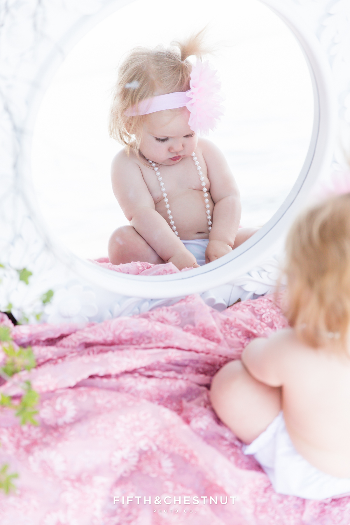 One year old girl playing with pearls and looking into mirror on Kiva Beach in Lake Tahoe