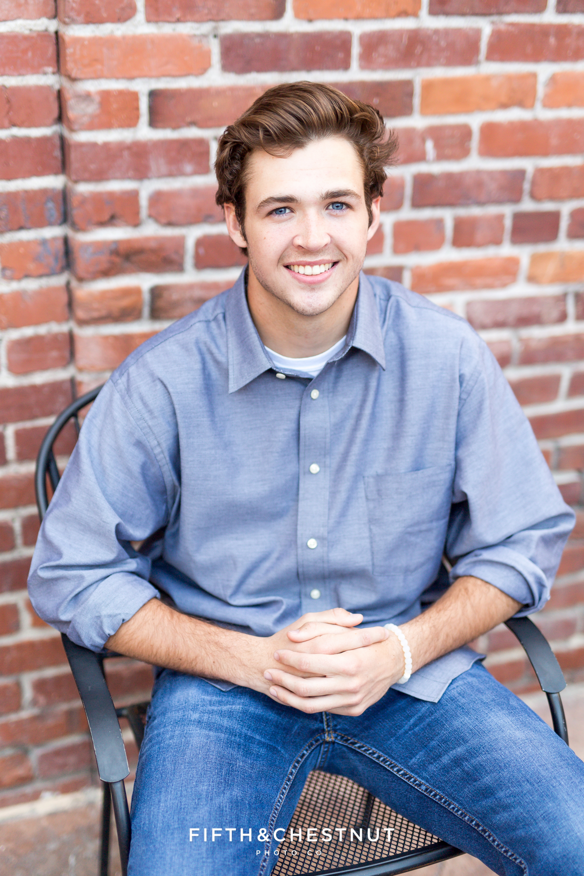 Reno High School Senior sitting in a chair in front of brick wall at West Street Market for his Reno Senior Portraits by Reno Senior Photographer