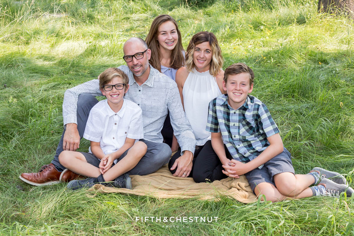 A family of five sits together on a yellow blanket on top of green grass in Tahoe Donner area