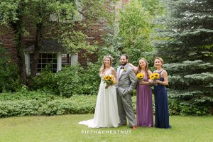 Bride, man of honor and bridesmaids dressed in royal blue and purple smile in front of the Twenty Mile House farm house for a photo by Graeagle Wedding Photographer