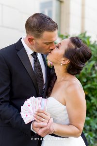Bride and groom hold playing cards that display their wedding date in Reno while kissing