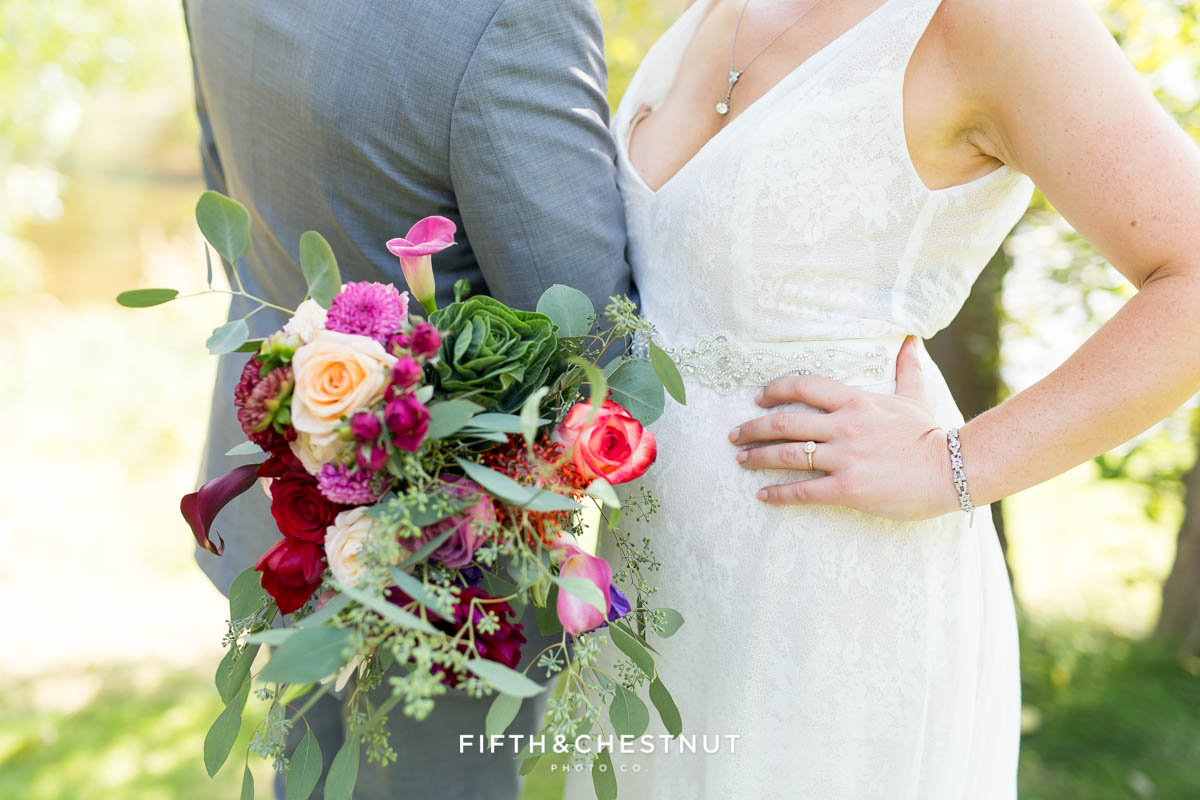 up close shot of bride with hand on hip, holding her bouquet alongside her groom wearing a gray suit for their bright and summery wedding bouquet for a Greenhorn Creek Guest Ranch Wedding