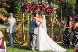 bride and groom kiss while horses rum wildly behind their ceremony site at their Greenhorn Creek Guest Ranch Wedding