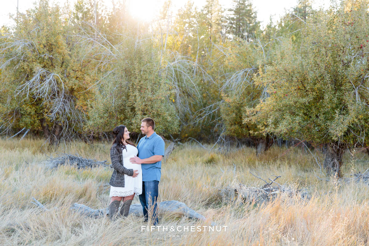 expecting couple looks at one another for their fall maternity portraits in an apple orchard field