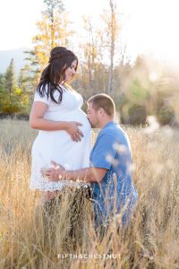 Husband down on one knee kissing his pregnant wife's pregnant tummy while the sun sets for their fall maternity portraits