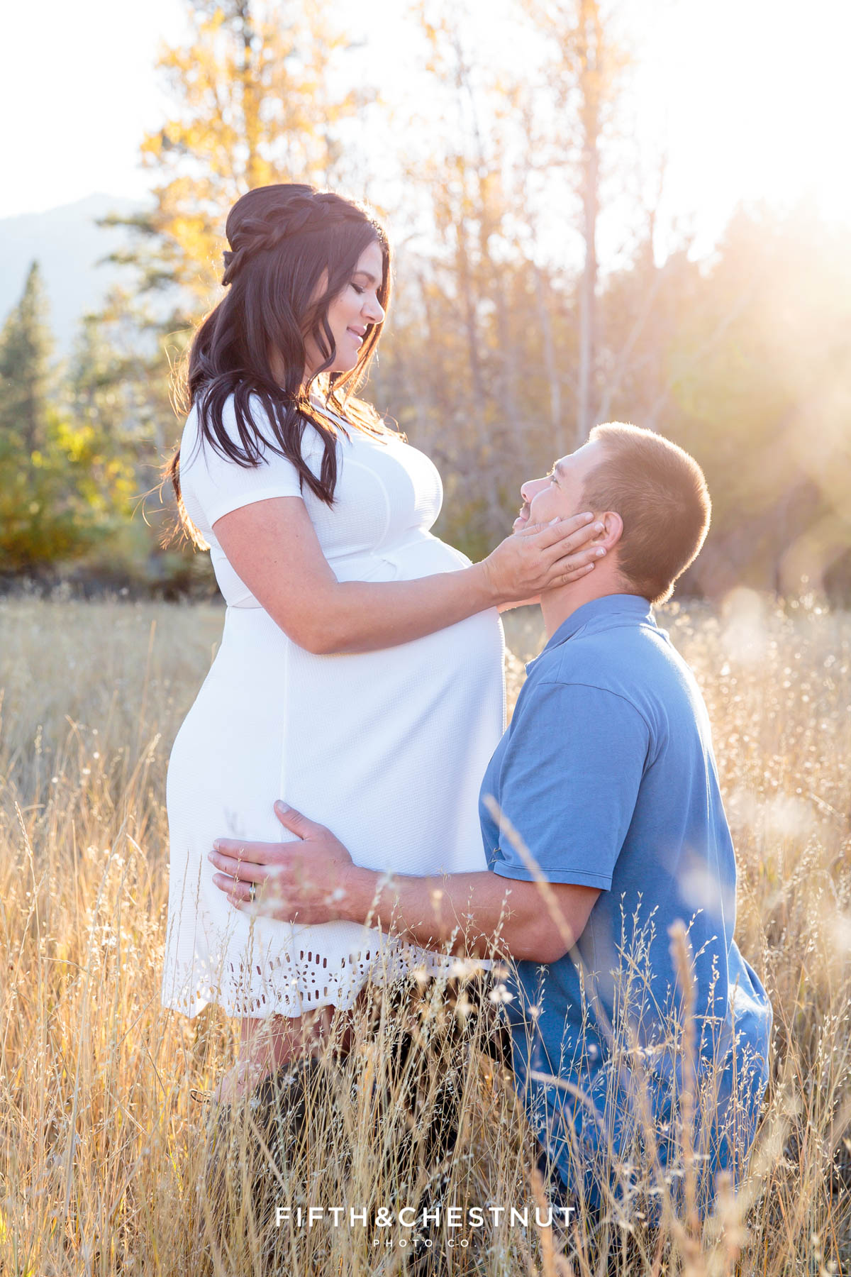 fall maternity portraits of husband kneeling down next to wife while she holds his cheek and looks lovingly into his eyes