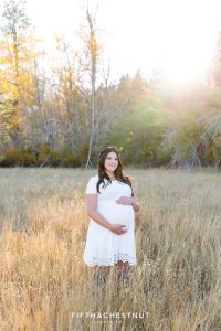 Pregnant woman in a white dress stands in a field for her fall maternity portraits