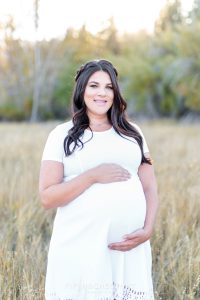 Pregnant woman in a white dress stands in a field for her fall maternity portraits