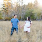 Couple stands apart and looks at each other while holding hands for their fall maternity portraits by Reno Maternity Photographer