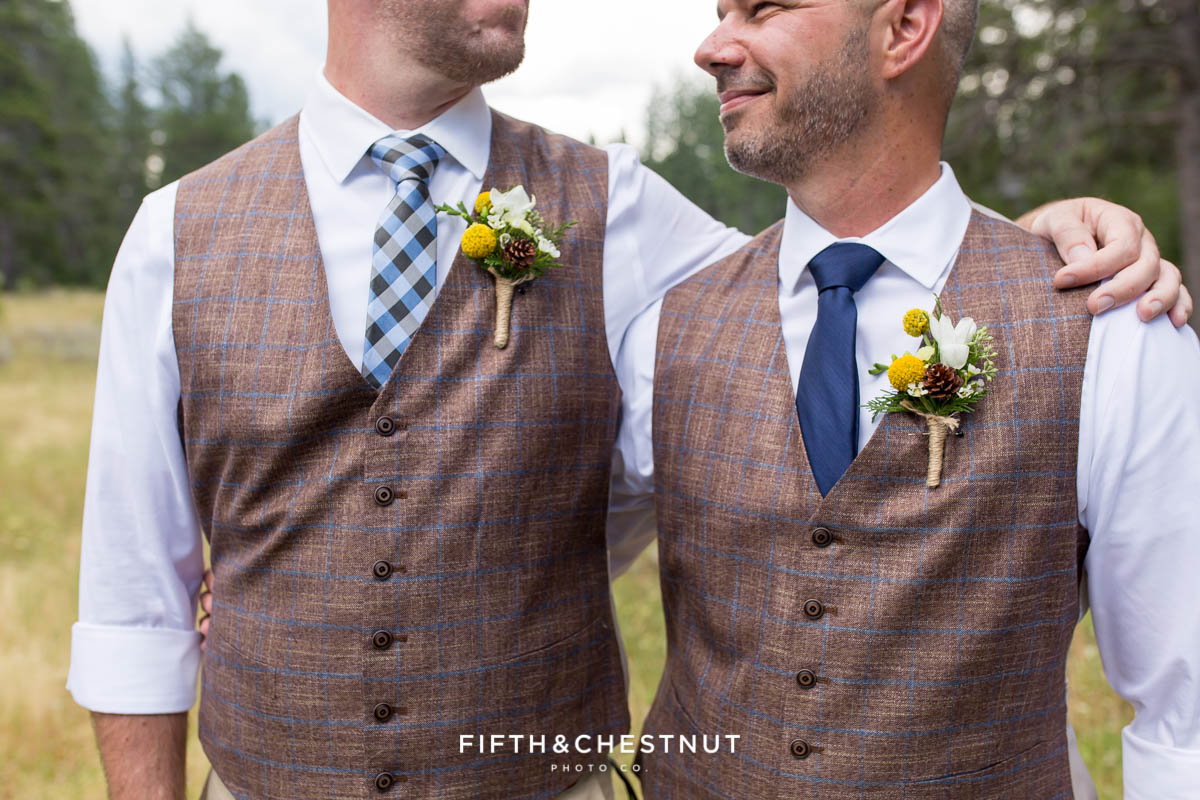 Two grooms stand side by side showing off their boutonnieres by Suzu's Petals before their gay wedding at PJ’s at Gray’s Crossing in Truckee