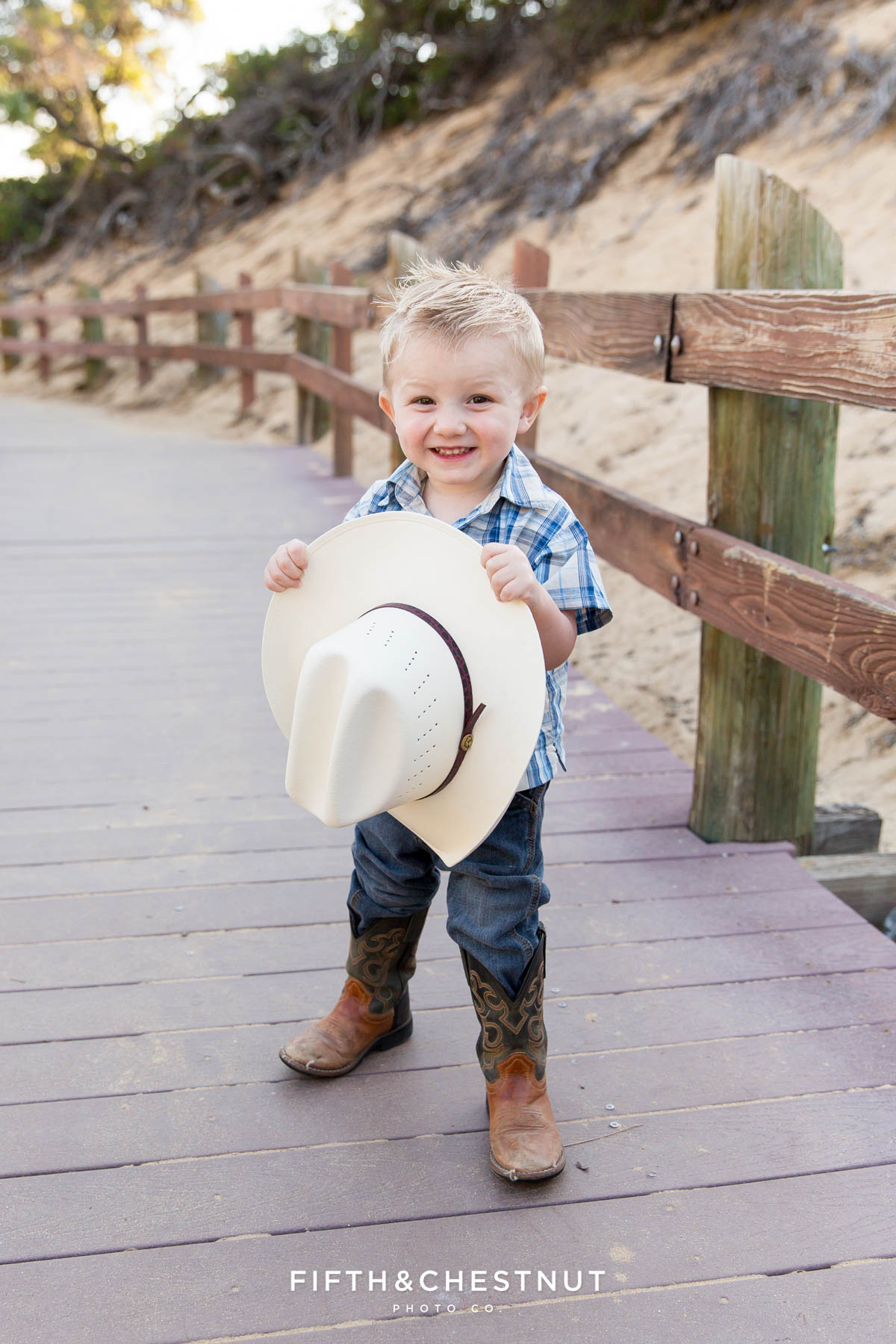 toddler holds cowboy hat wearing a plaid shirt at Sand Harbor