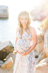 beautiful mama holds her pregnant belly in front of rocks and water for Tahoe Maternity Portraits