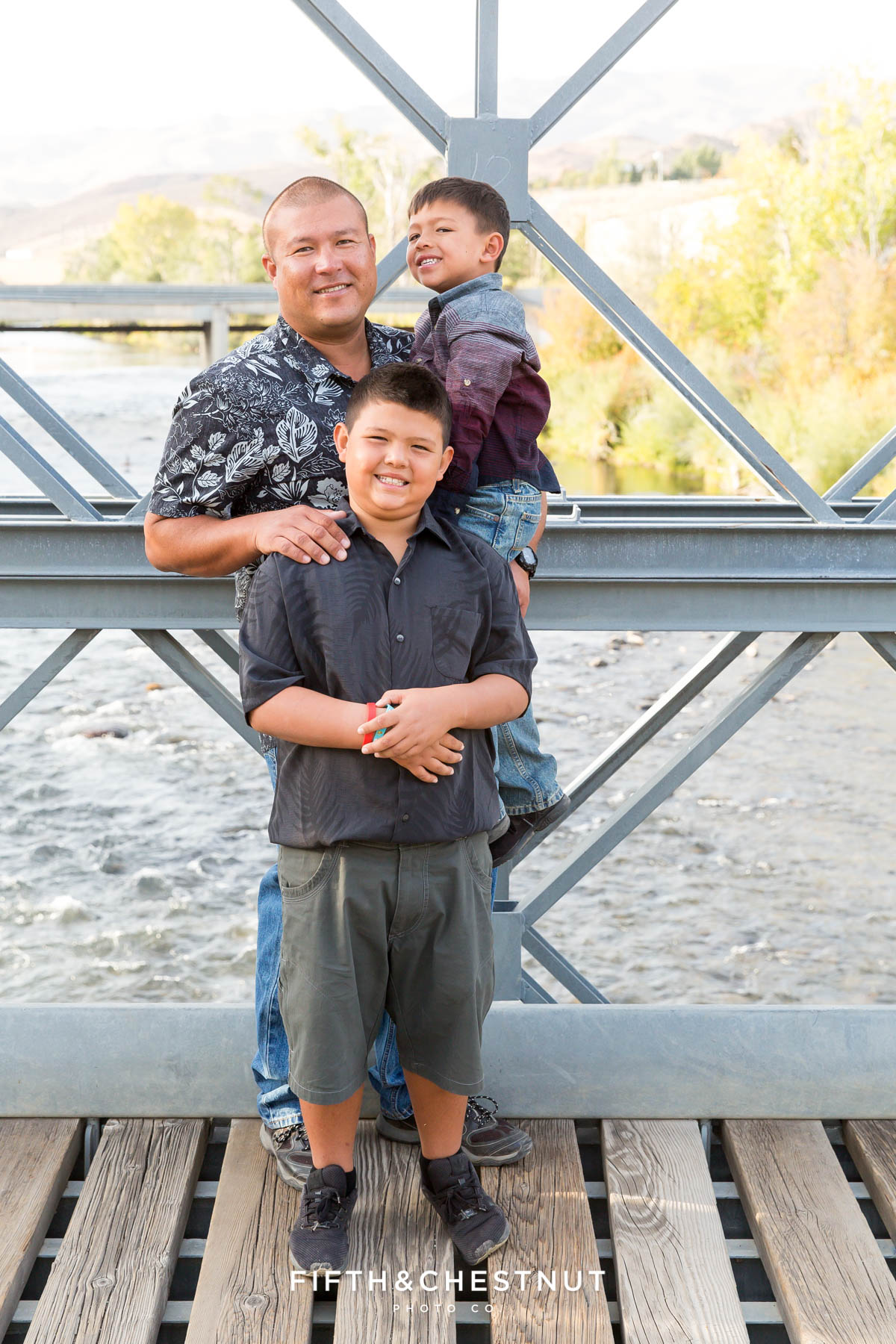 father and sons pose on a bridge for vibrant fall  portraits at Mayberry Park