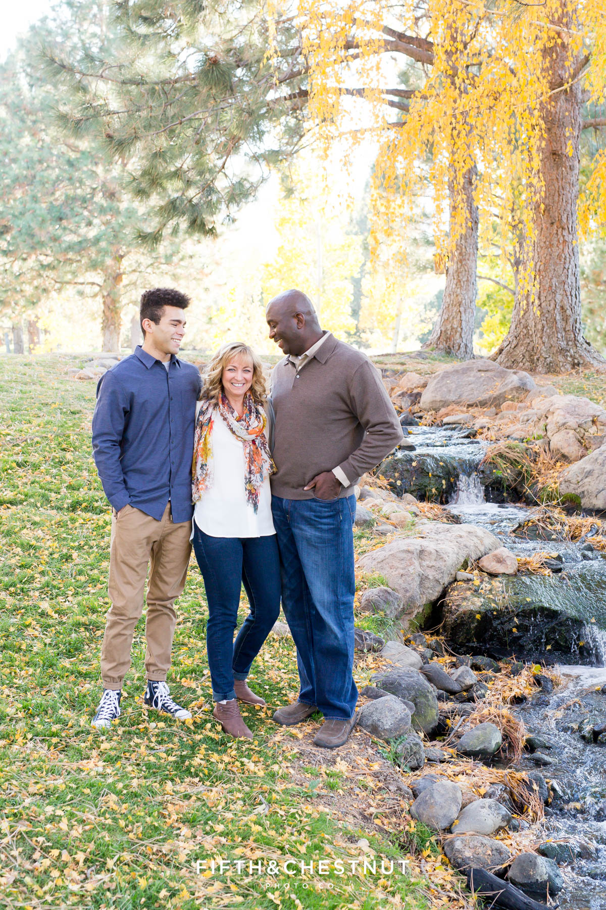 family of three stand by creek and laugh during their fall family portraits at Caughlin Ranchfall family portraits at Caughlin Ranch by Reno Family Photographer