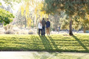 Family of three stands across a pond for fall family portraits at Caughlin Ranch