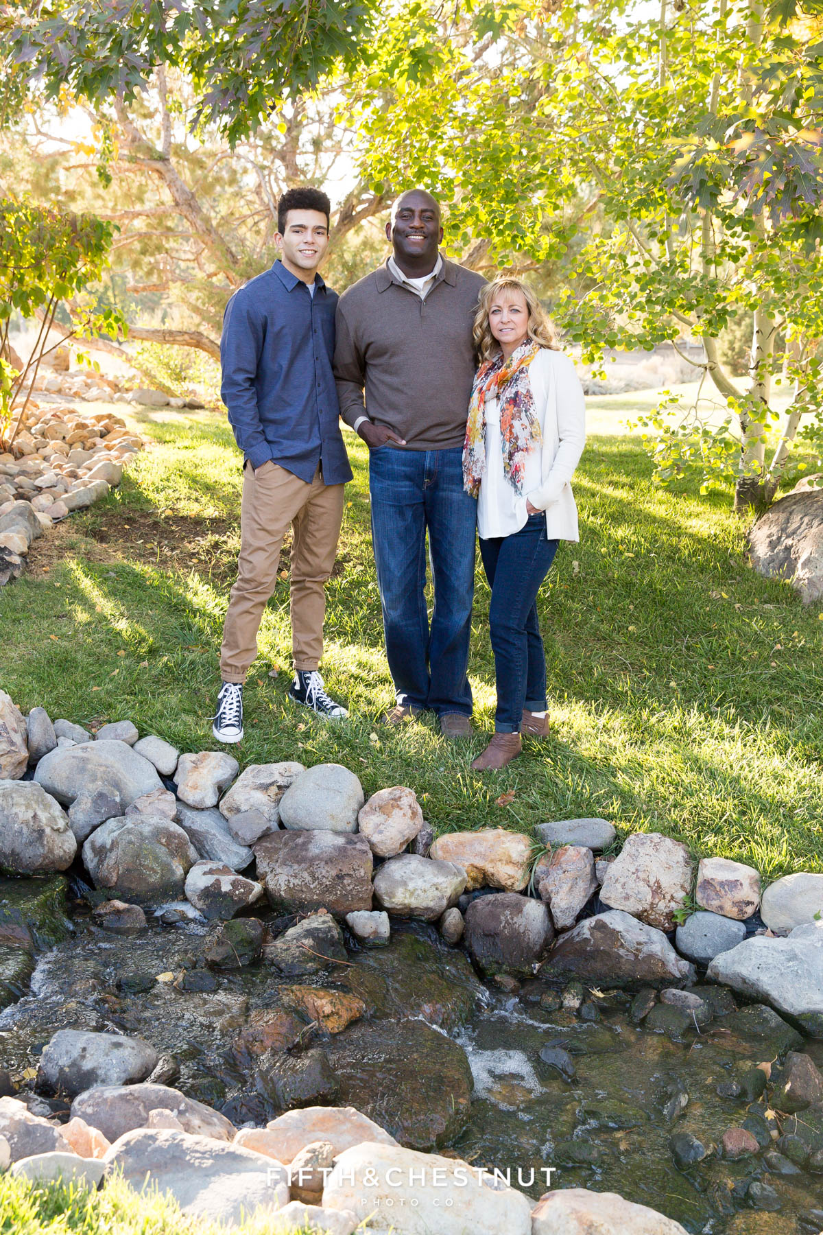 family of three stand near creak and simile for their fall family portraits in Reno
